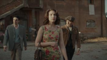 The Monster of Florence TV show screenshot 1: A woman wearing a floral dress walks through an Italian town with two men walking behind her in suits