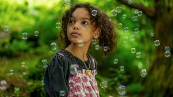 The Primrose Railway Children: Phoebe looks to left, curiously. She wears pigtails and there are soap bubbles floating in front of her.