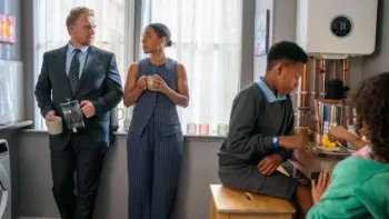 The Primrose Railway Children: Inside a modern kitchen, Mom and Dad look at each other in formal clothes by the window. Perry and Phoebe eat breakfast