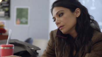 True Lies TV show: Helen holds cell phone to ear with shoulder while sitting in her classroom.