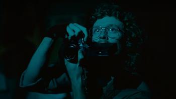 True Haunting TV show screenshot 3: A man with curly hair and 1980s-style metal aviator glasses holds a camera up in front of his face