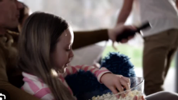 TV We Love TV show screenshot 1: A little girl in pink and white striped shirt eatting popcorn while man holds remote