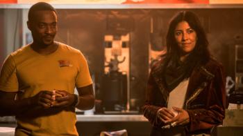 Twisted Metal: John and Quiet are shown together in front of a chalkboard. Both are smiling and look to be holding small white cards. 