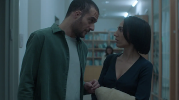 Unconditional TV show screenshot 2: A man and woman talk in a dimly lit hallway.