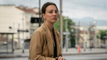 Vanished TV show screenshot 1: Kaley Cuoco sands in the middle of a street. She wears a tan coat and black shirt.