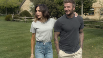 Victoria Beckham TV show screenshot 3: Victoria Beckham in gray shirt walks with David Beckham in blue shirt.