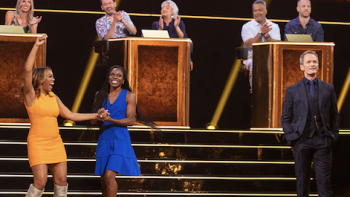 What's in the Box TV show screenshot 3: Contestants sit and clap while two stand and celebrate on steps.