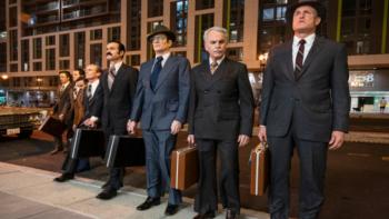 White House Plumbers TV show: Eight men in 1960s-era suits and hats and with briefcases stand in a line on a curb with a city background. Hunt, Liddy, Sturgis, and other Watergate conspirators are visible. 