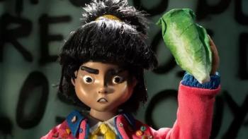 Women Wearing Shoulder Pads TV show screenshot 3: Nina stands in front of a graffiti-covered wall, wearing a pink jacket and waving lettuce in the air