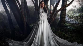 Yaga TV show screenshot 1: Katherine is seen against a background of shadowy trees, wearing a long white dress that flows onto the ground