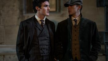 Young Sherlock TV show: Dónal Finn and Hero Fiennes Tiffin. Finn wears a striped suit. Tiffin wears a cap, striped vest, and a dark coat.