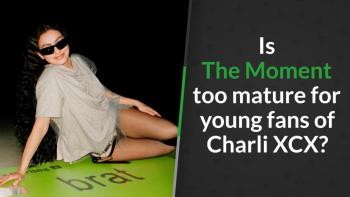 Charli XCX wearing sunglasses reclines on a large green credit card prop beneath
