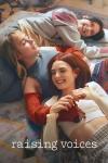 Raising Voices: Three teenage girls lay on each other on a bed smiling.