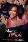 She the People TV Poster: Terri J, Vaughn waves in a crowd of men in suits. She wears a pink jacket with an American flag pin.